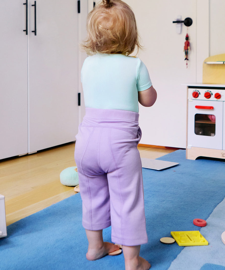 Child wearing a short sleeve baby onesie in glacier blue and purple leggings, looking away from the camera.