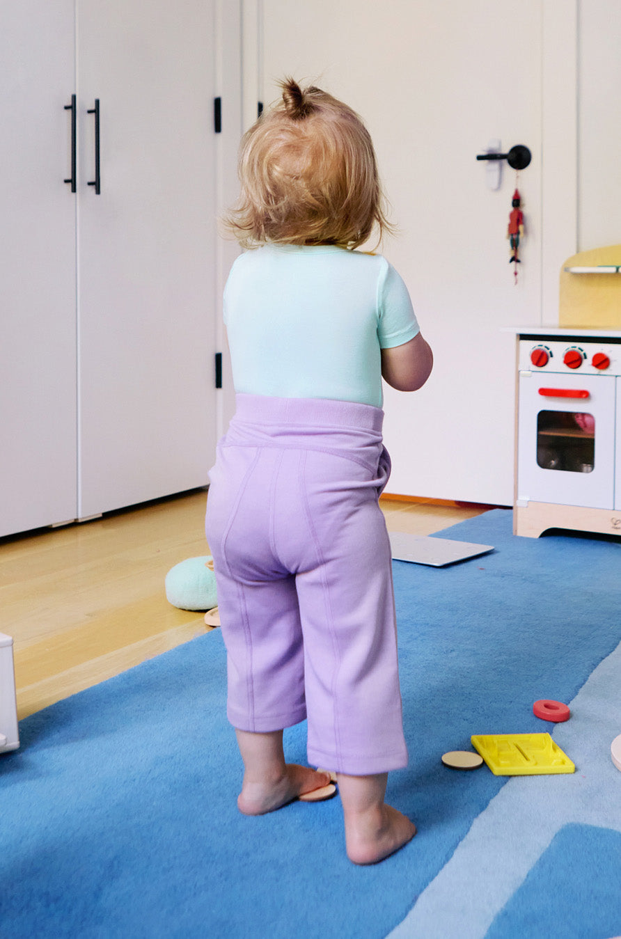 Child wearing a short sleeve baby onesie in glacier blue and purple leggings, looking away from the camera.