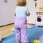 Child wearing a short sleeve baby onesie in glacier blue and purple leggings, looking away from the camera.