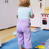 Child wearing a short sleeve baby onesie in glacier blue and purple leggings, looking away from the camera.