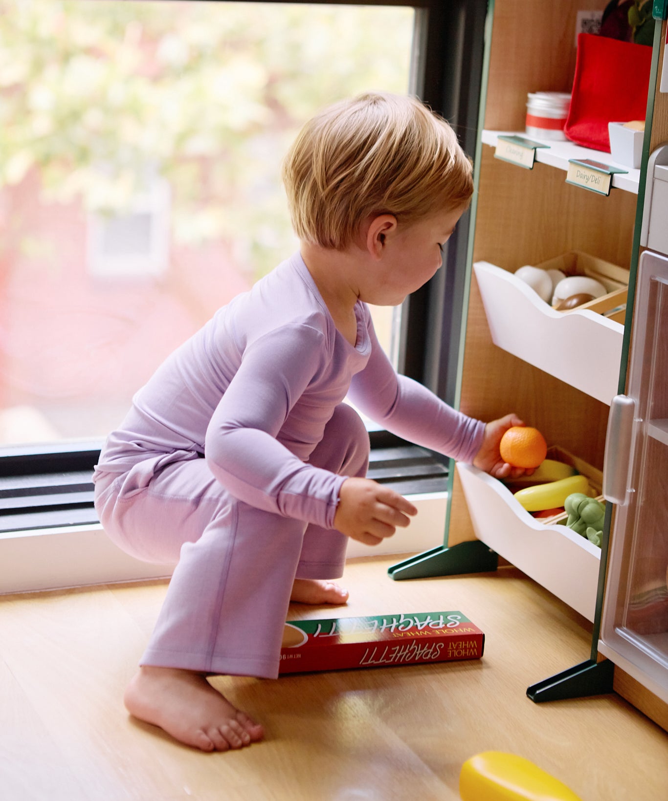 Girl playing with toy fruits while wearing a long sleeve kid's t-shirt and straight pant bundle in lilac