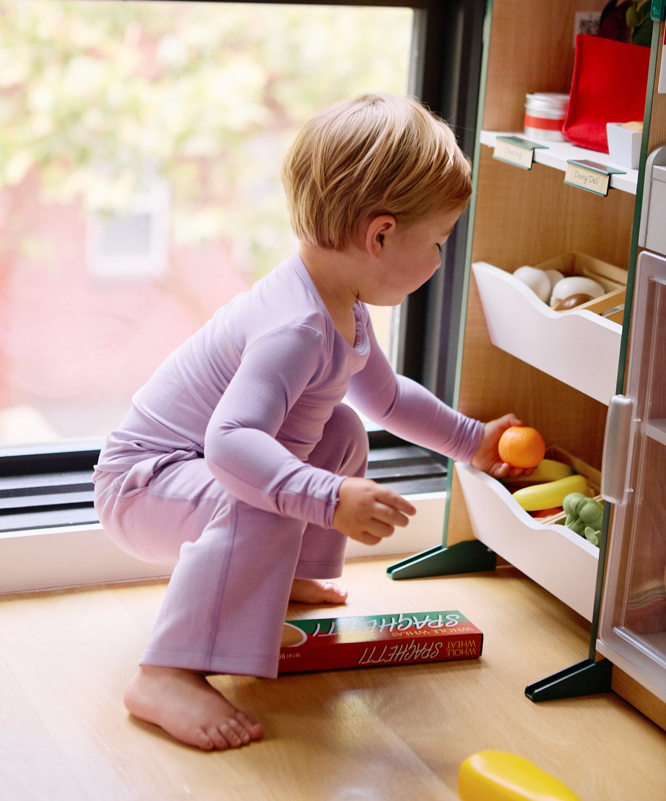 Girl playing with toy fruits while wearing a long sleeve kid's t-shirt and straight pant bundle in lilac